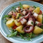 Insalata di polpo e patate servita su piatto rustico con rucola e limone