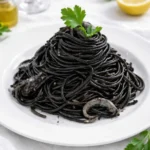 Pasta al nero di seppia con seppie e prezzemolo, servita calda su piatto bianco