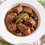 Spezzatino di manzo servito con olive e rosmarino in un piatto fondo bianco.
