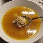 Ciotola di Brodo di Pesce Persico dorato su piano cucina con cucchiaio