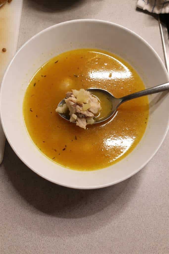 Brodo di Pesce Persico in ciotola bianca con cucchiaio e pezzi di pesce in primo piano