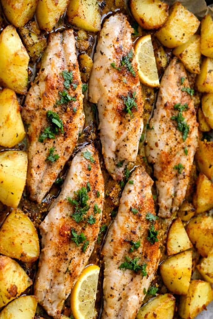 Pesce persico al forno con patate arrosto, limone e prezzemolo fresco su teglia