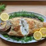Pesce persico al sale con crosta rotta servito su piatto ovale con limone e aneto