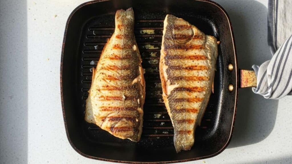 Filetti di pesce persico alla piastra con segni di griglia dorati su piastra in ghisa nera