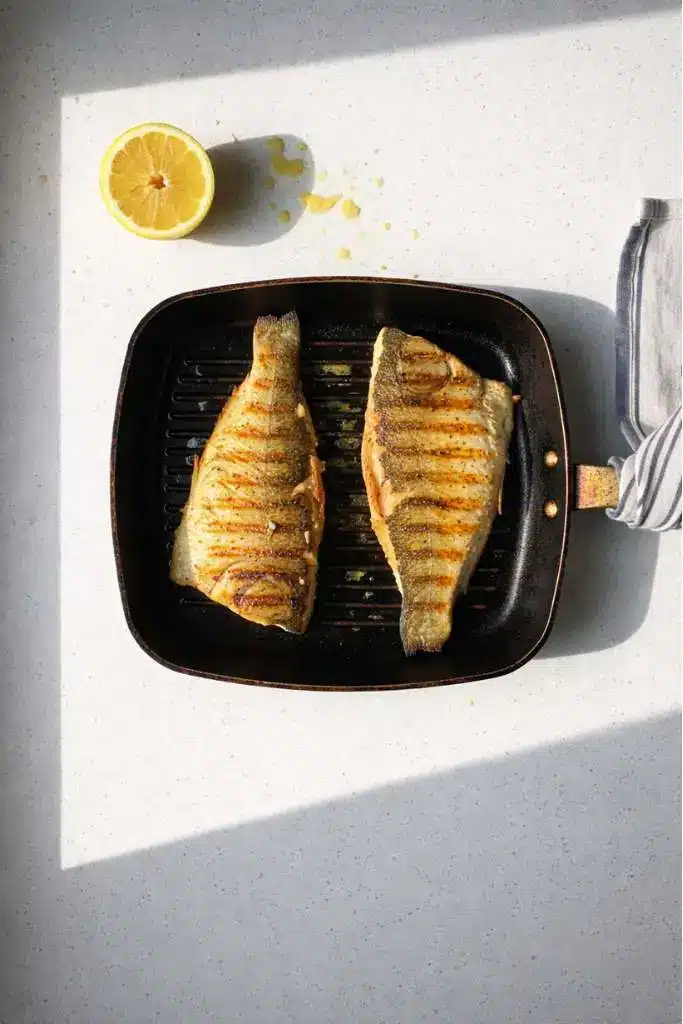Pesce persico alla piastra con segni di griglia su piastra in ghisa nera e limone