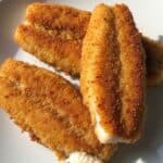 Pesce persico fritto dorato e croccante su piatto bianco con limone