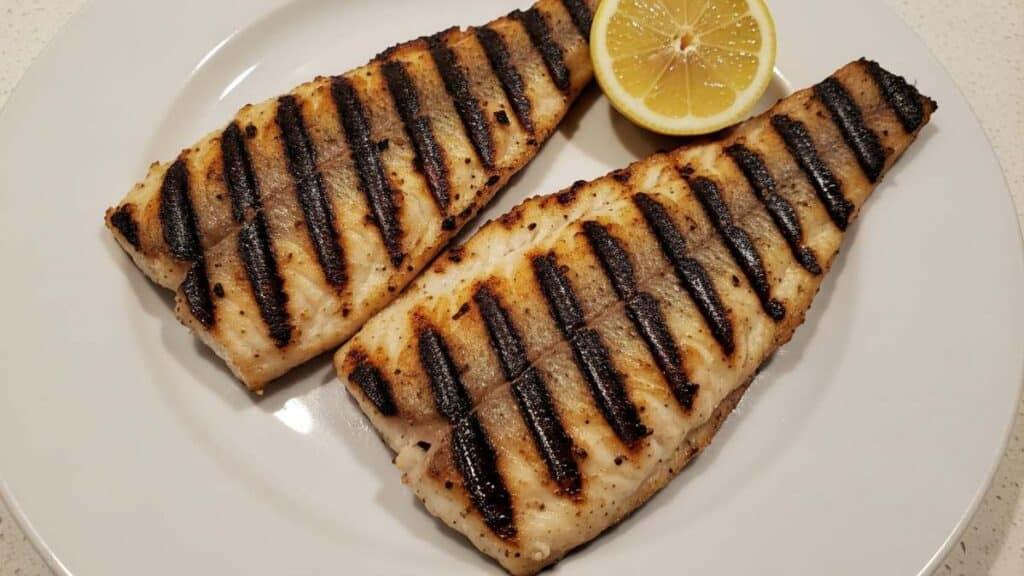 Filetti di pesce persico grigliato alla piastra con segni della griglia e limone su piatto bianco