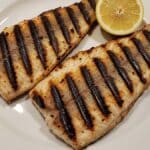 Filetti di pesce persico grigliato alla piastra con segni della griglia e limone su piatto bianco