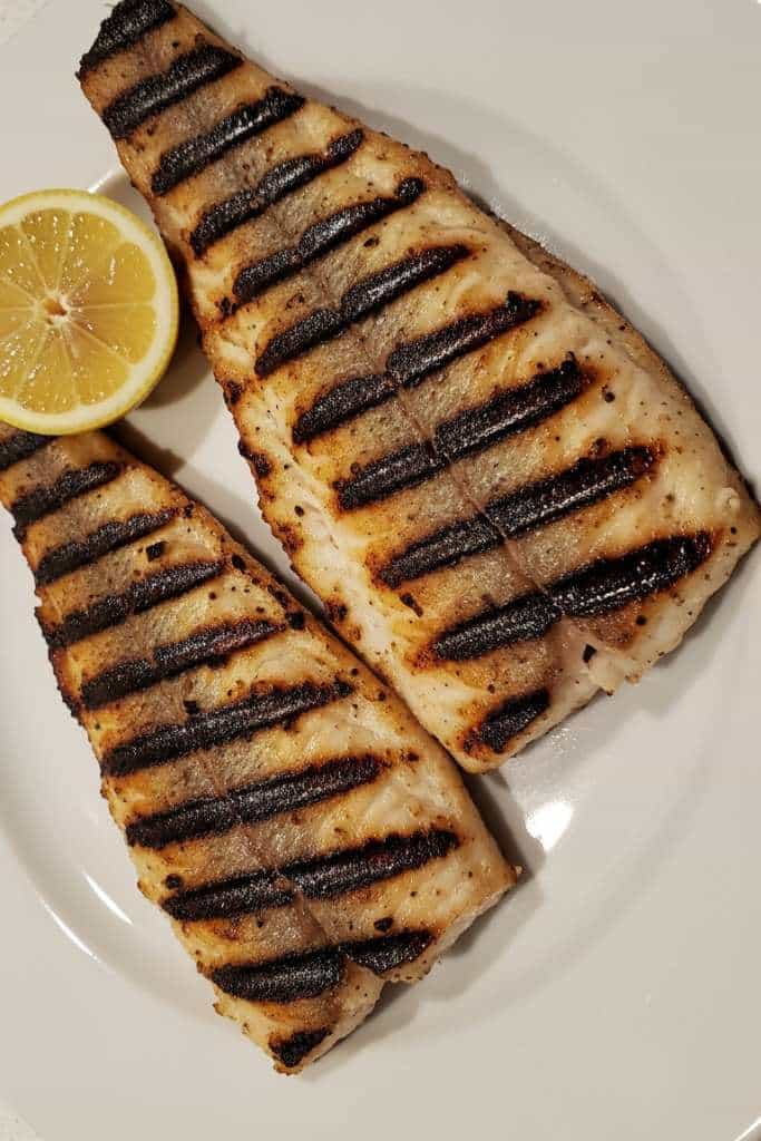 Due filetti di pesce persico grigliato con evidenti segni della griglia su piatto bianco