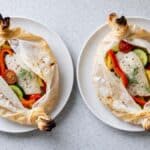 Pesce Persico in Cartoccio con zucchine, peperoni e pomodorini servito su piatti bianchi