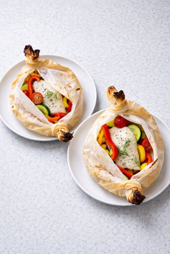 Pesce Persico in Cartoccio con verdure fresche in carta forno su piatti bianchi formato verticale