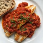 Pesce persico in umido con salsa di pomodoro e pane casereccio su piatto bianco
