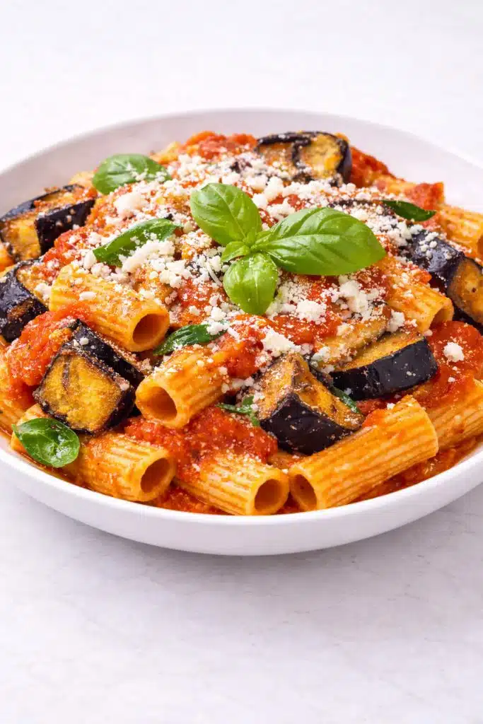 Pasta alla Norma con melanzane fritte ricotta salata e basilico su piatto bianco