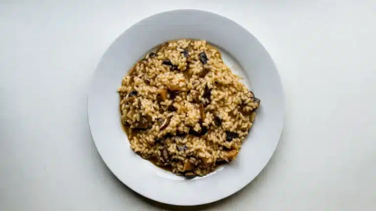 Risotto ai funghi porcini cremoso servito su piatto bianco visto dall’alto