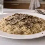Risotto al tartufo cremoso con lamelle di tartufo nero su piatto bianco