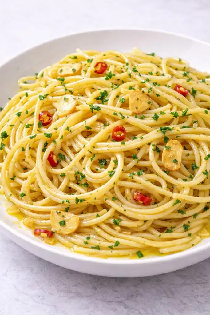 Spaghetti aglio olio e peperoncino con aglio peperoncino e prezzemolo su piatto bianco